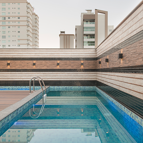 piscina do residencial lago negro construído pela itapuí incorporadora. Na imagem é possível ver uma piscina em formato de L, em um ambiente charmoso com pisos e revestimentos nas cores, marrom, creme e outros tons terrosos.